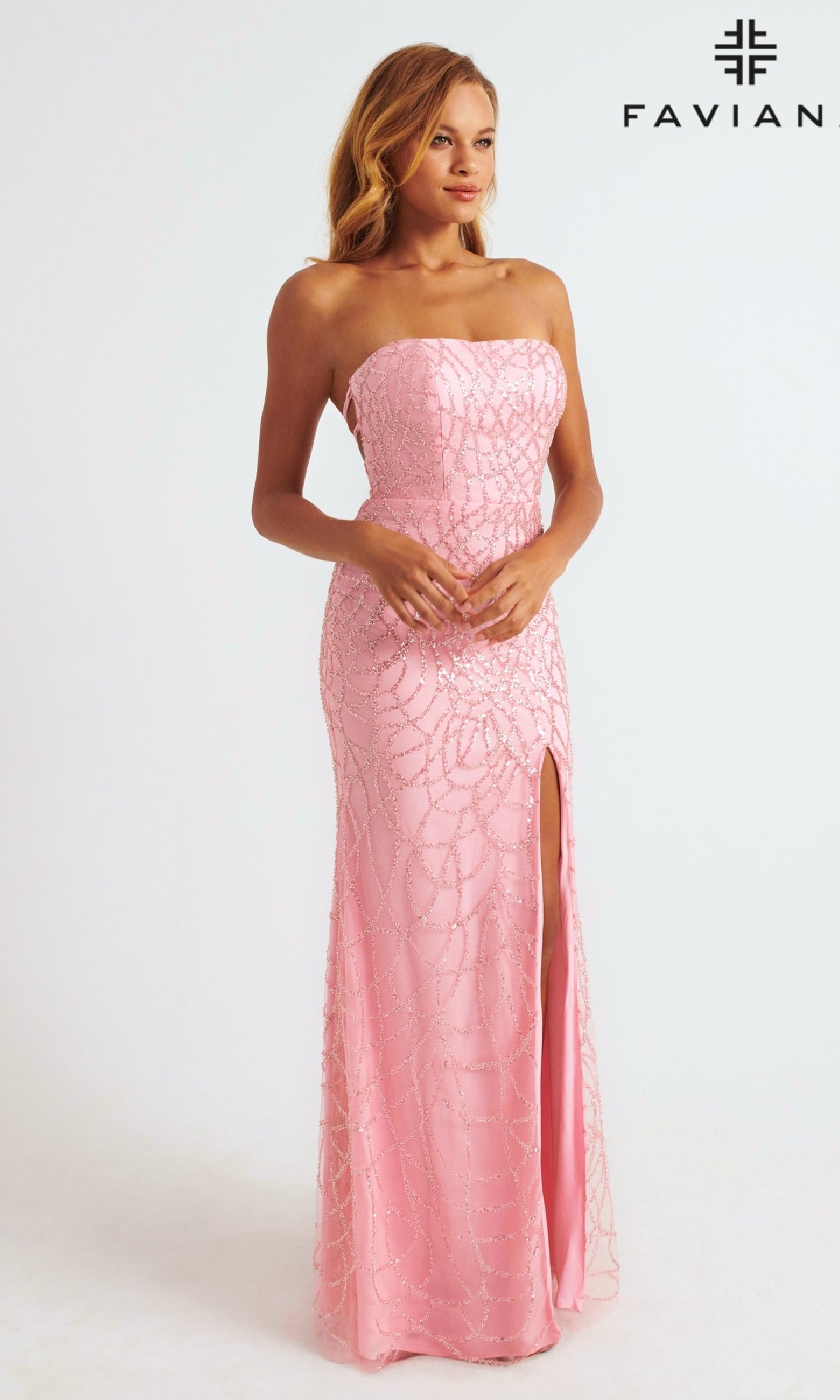 A woman in the Strapless Faviana Long Glitter-Print Prom Dress, a light pink gown with a thigh-high slit and sparkling details, stands before a plain background; the FAVIAN logo appears in the top right corner.